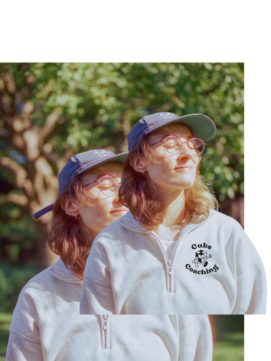 A calm person smiling wearing glasses and a baseball cap in nature in the sun